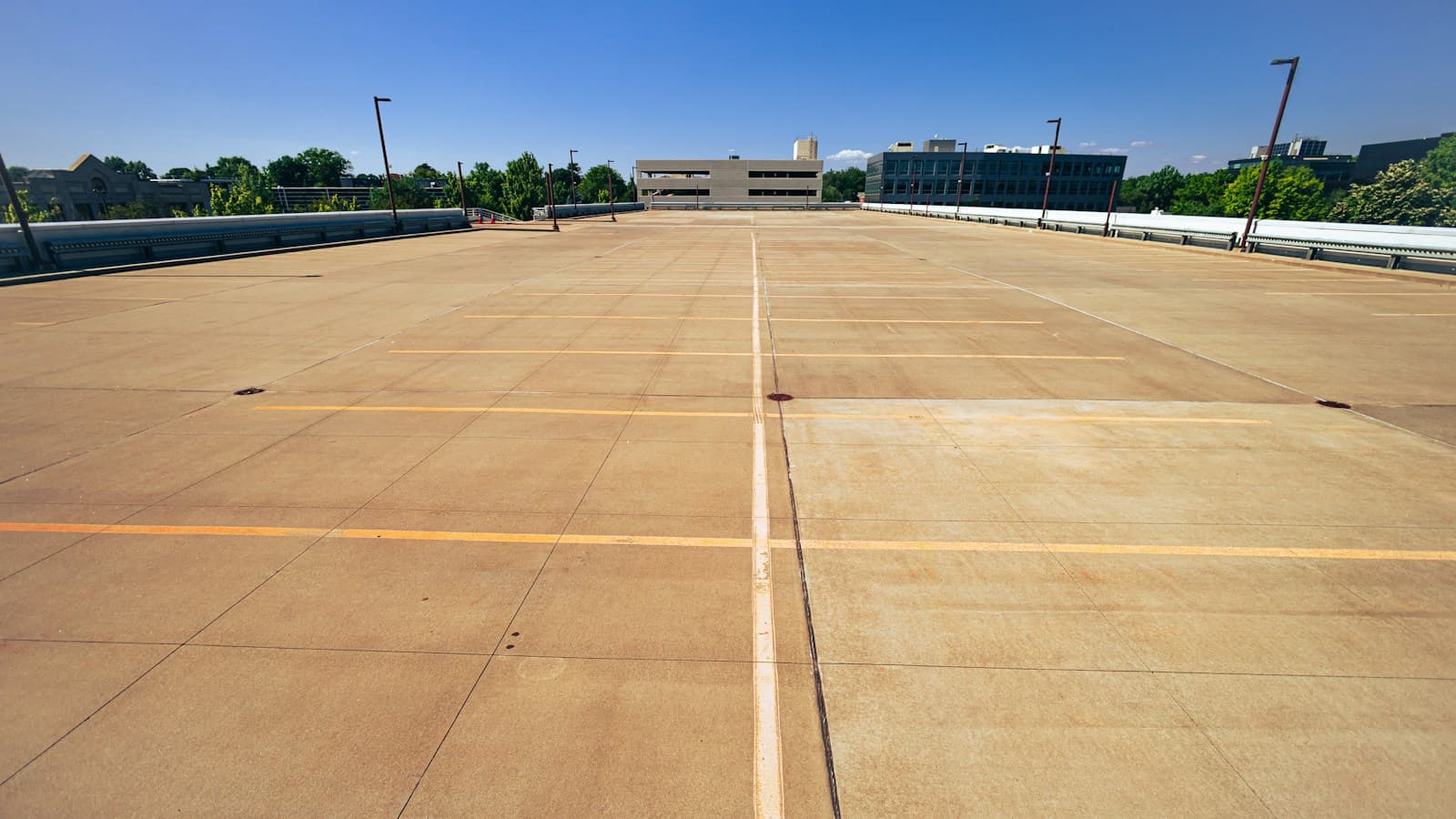 A mostly empty open-air parking deck with dry marked spaces, nearby green trees, and a clear blue sky.
